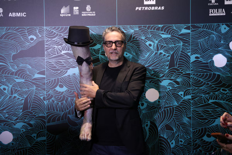 Kleber Mendonça Filho, diretor de O Agente Secreto, posa com a prótese da Perna Cabeluda utilizada no filme 