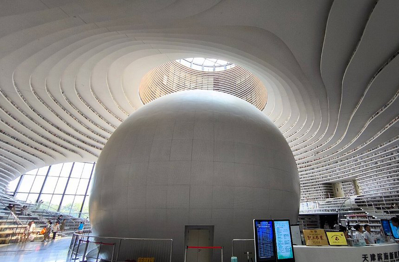 A luz natural invade o átrio e reflete nas superfícies brancas, construindo um ambiente que parece suspenso entre sonho e realidade. O “olho” central funciona como farol de cultura e encontro, guiando passos curiosos rumo às estantes onduladas. À noite, a iluminação deste templo futurista do conhecimento cria atmosfera quase cósmica. 
