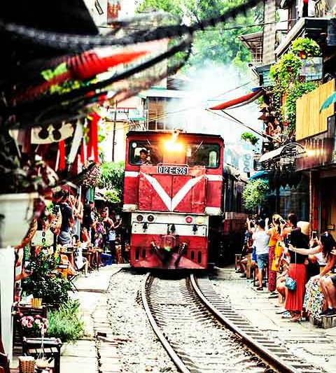 Antigas casas foram convertidas em cafeterias, onde visitantes aguardam a passagem do trem a apenas 10 km/h enquanto consomem bebidas.