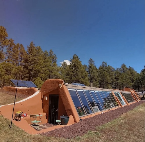 A casa fica parcialmente enterrada e conta com uma grande fachada de vidro que permite climatização natural.