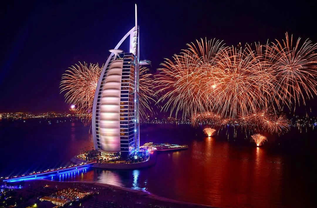 À noite, a fachada translúcida reflete luzes coloridas, criando o efeito de uma vela que muda de cor sob o céu árabe.