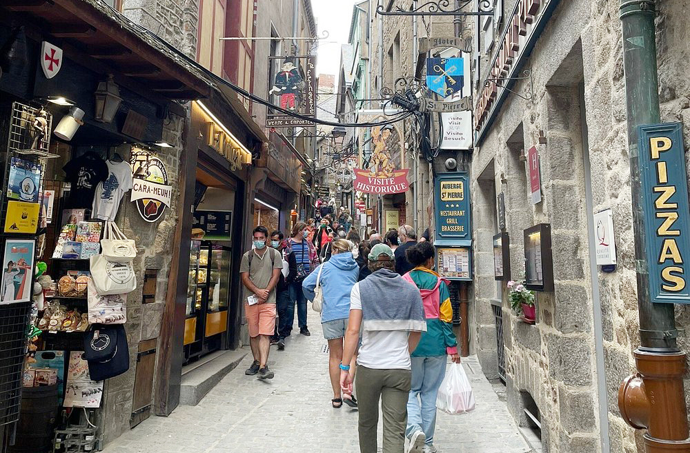A Grand Rue é a rua principal, repleta de lojinhas, cafés e restaurantes. Apesar de turística, mantém o charme medieval com fachadas de madeira e placas antigas. É comum encontrar produtos típicos da Normandia, como cidra, caramelo de manteiga salgada e lembranças religiosas.