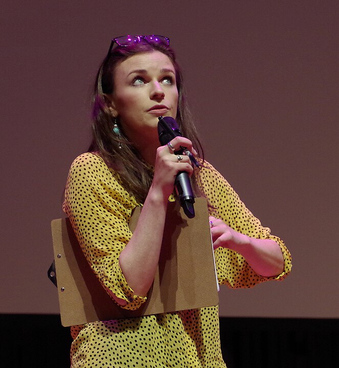 Aisling Bea – Nascida em 1984, em Condado de Kildare, é atriz, roteirista e comediante. Criadora e estrela da série This Way Up, elogiada pela crítica, também participou de Living with Yourself e Greatest Days, destacando-se pela inteligência e humor afiados.