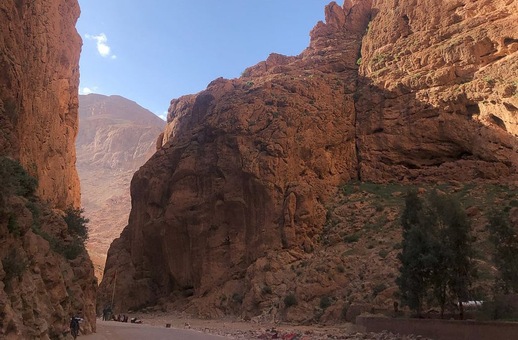 As paredes verticais da Garganta de Todra parecem esculpidas à mão, formando um corredor natural entre montanhas de pedra avermelhada. O contraste entre o céu azul e as rochas alaranjadas cria uma atmosfera quase surreal. É como caminhar por um templo aberto, onde cada curva revela uma nova perspectiva.