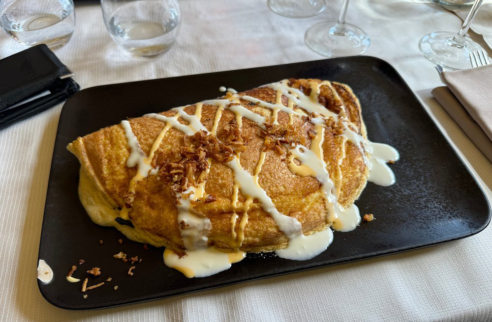 <p>A omelete da Mère Poulard é uma tradição local desde 1888. Feita com ovos batidos vigorosamente até virar espuma, é cozida em fogo de lenha. O restaurante original ainda funciona e atrai turistas do mundo todo. O preço é salgado, mas a experiência é única.</p>
