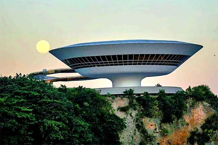 <p>O projeto de Oscar Niemeyer para o Museu de Arte Contemporânea de Niterói tem vista para a Baía de Guanabara. Além disso, possui forma de disco e a rampa vermelha que criam uma silhueta de ficção científica que parece flutuar sobre a costa.</p>
