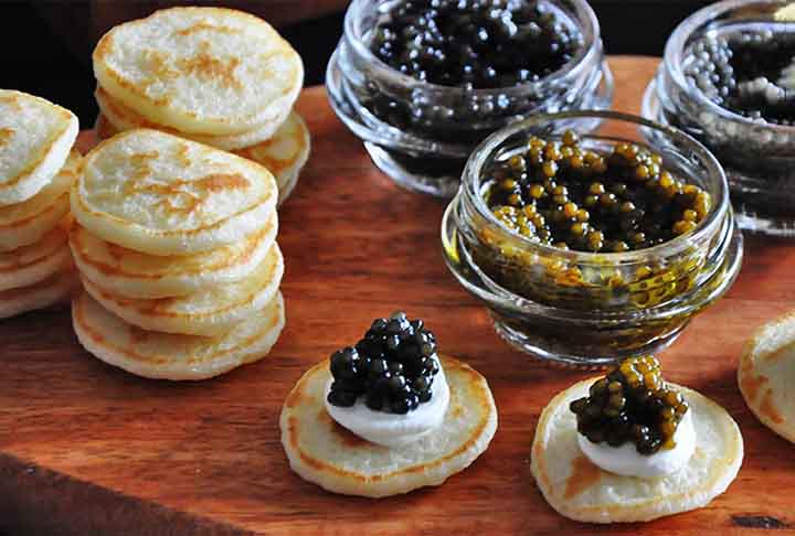 <p>As panquecas russas, ou Blini, são finas e pequenas, tradicionalmente feitas com uma mistura de trigo e centeio, muitas vezes fermentada. São servidas com manteiga, caviar, smetana (creme azedo) ou mel. Blini têm uma textura mais densa e sabor levemente azedo devido à fermentação.</p>
