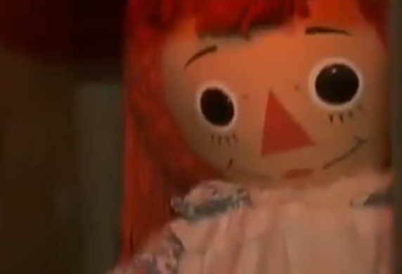 Essa boneca era de pano, com olhos escuros, cabelos avermelhados e um sorriso. 