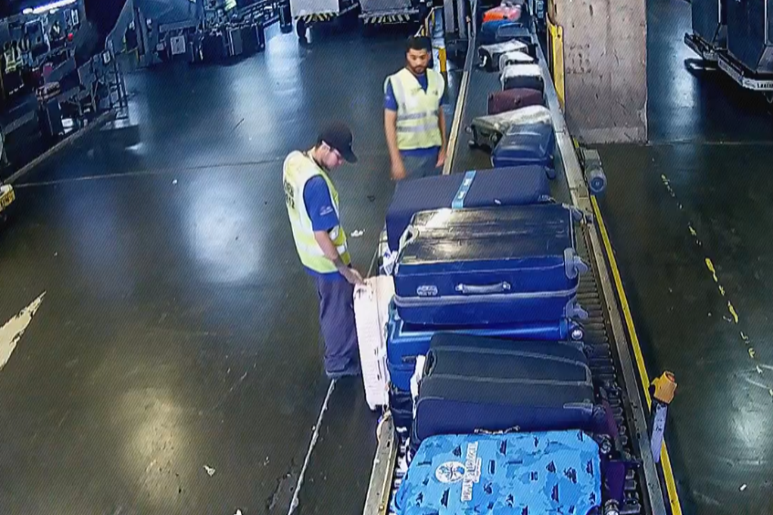 Pedro Venancio confere a etiqueta da mala, enquanto o comparsa o observa.