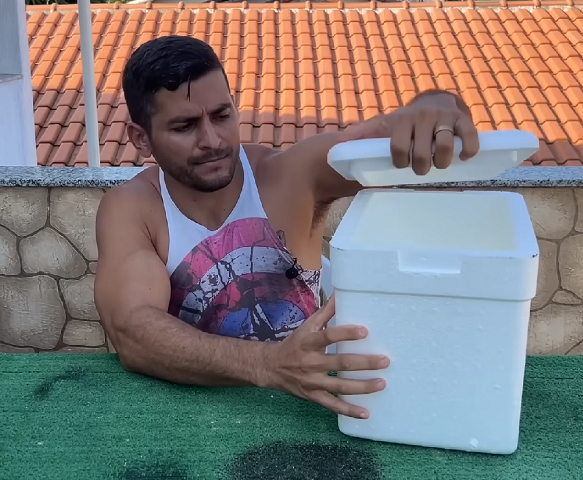 No tutorial, um homem usa uma caixa de isopor como a base dessa solução improvisada, mas também menciona que um pote ou balde com tampa pode ser utilizado. 