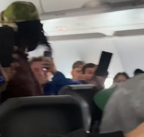 Outros passageiros se levantam e correm para o corredor para fugir enquanto a mulher avança.