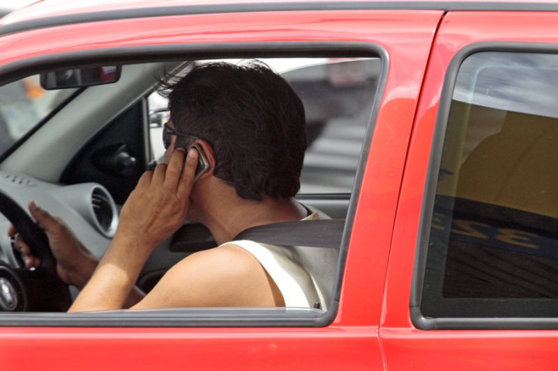 Homem utilizando telefone celular durante a condução do veículo.