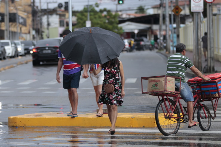 a chuva mostra duas pessoas atravessando a rua, uma de guarda-chuva e outra sem. TambÃ©m hÃ¡ um ciclista no lado direito da foto